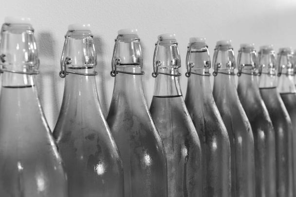 Ασπρόμαυρη φωτογραφία μιας σειράς από μπουκαλάκια σπιτικού μηλίτη καλυμμένα με συμπύκνωση - Φωτογραφία, εικόνα