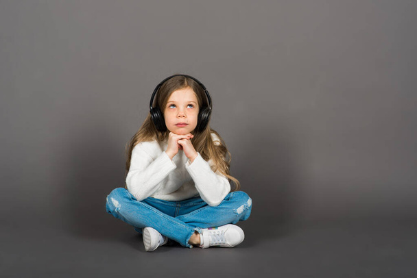 Linda niña en auriculares disfrutando de música de baile feliz, sonrisa, posando en la pared de fondo del estudio gris. - Foto, Imagen