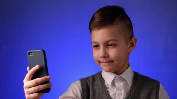 Um rapaz da escola bonito tira uma selfie no telemóvel. Criança moderna é fotografada em seu smartphone. - Filmagem, Vídeo