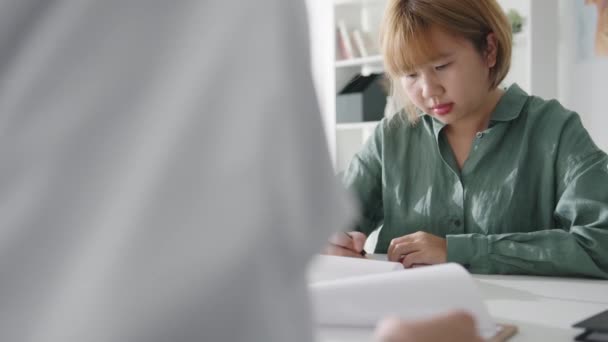Genç Asyalı kız hasta sağlık sigortası formunu imzalıyor ya da klinikte beyaz üniformalı bayanla sağlık hastanesi ofisinde masasında otururken sağlık sigortası sözleşmesi imzalıyor.. - Video, Çekim