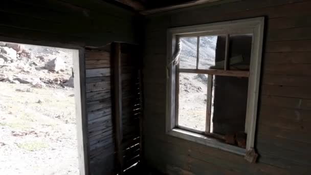 Pohled okny do opuštěného dřevěného domu. Klip. Stará zřícenina dřevěné budovy a svah kopce venku. - Záběry, video