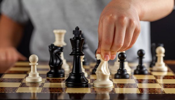 白人の少年が試合中に白い騎士のチェス駒を持っている。彼は移動します。決定、集中、集中、行動概念を取るリスクの計算のための暗い背景画像 - 写真・画像