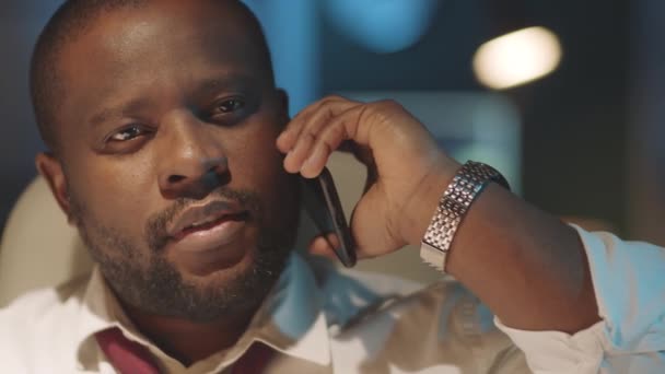 Chest up shot de empresario negro positivo hablando en el teléfono móvil en la oficina oscura, mientras que el trabajo de horas extras en la noche - Metraje, vídeo