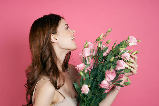 gyönyörű nő egy csokor virág egy rózsaszín háttér egy könnyű ruha smink modell - Fotó, kép