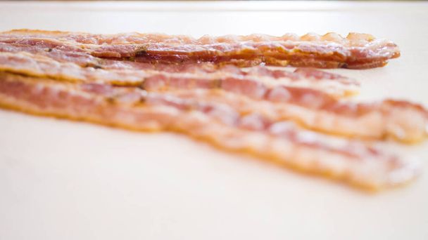 Slicing bacon strips into bacon bits on a white cutting board. - Photo, Image