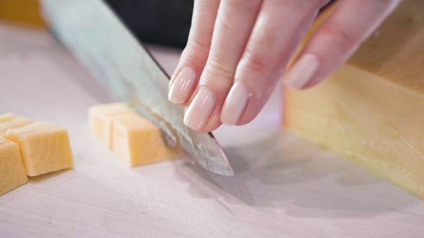 Slicing gouda cheese into small cubes on a white cutting board. - Photo, Image