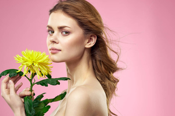 Hermosa chica con una flor amarilla sobre un fondo rosa maquillaje hombros desnudos - Foto, Imagen
