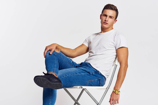 Man on a chair indoors torn jeans white t-shirt handsome face model light background - 写真・画像