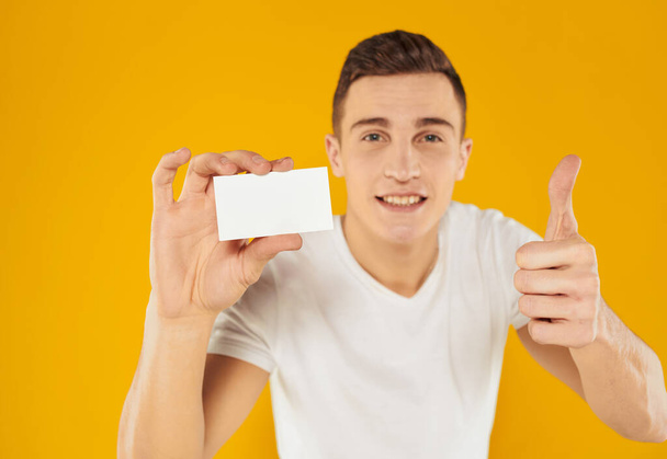 guy in white t-shirt showing business card on yellow background cropped view - Foto, Imagem