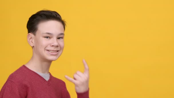 Lustige Teen Boy Gestik Rock Zeichen zeigt Zunge, gelber Hintergrund - Filmmaterial, Video