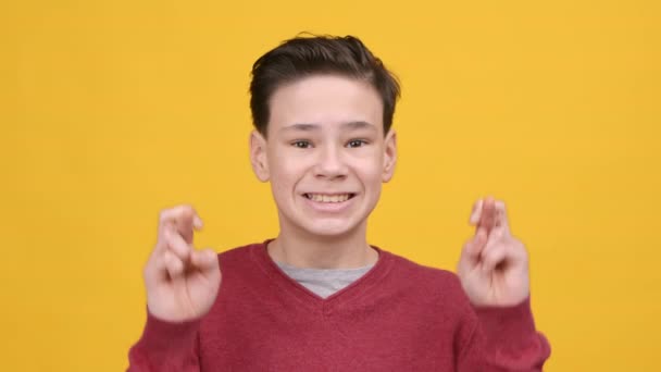Мальчик держит пальцы скрещенными на удачу на жёлтом фоне - Кадры, видео