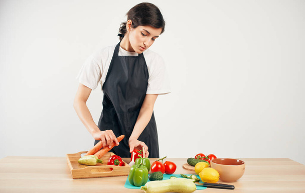 Mujer chef en delantal negro rebanando verduras cocina comida sana hogar - Foto, imagen