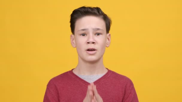 Niño adolescente rezando sosteniendo las manos en el gesto de oración, fondo amarillo - Imágenes, Vídeo