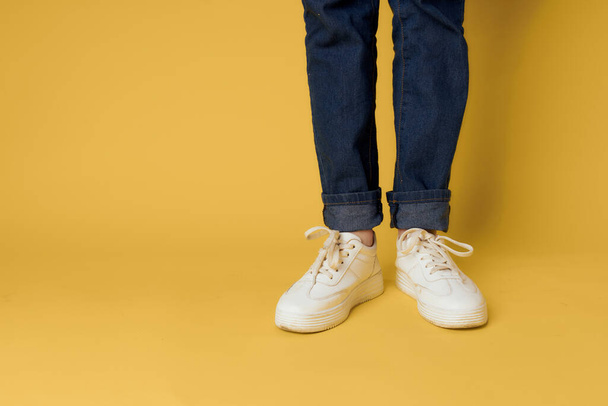 Vrouwen benen jeans witte sneakers mode straat stijl gele achtergrond - Foto, afbeelding