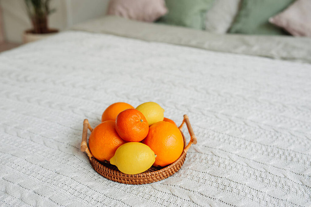 dużo owoców cytrusowych pomarańcze, mandarynki i cytryny na drewnianej wikliny eco taca na lekkiej dzianiny koc na przytulnym łóżku w stylu boho. zdrowe odżywianie i wzmacnianie, selektywne ukierunkowanie - Zdjęcie, obraz