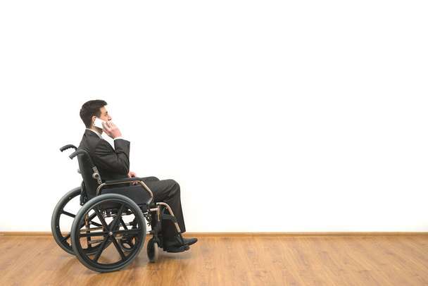 Los discapacitados en una silla de ruedas teléfonos en el fondo blanco de la pared - Foto, imagen