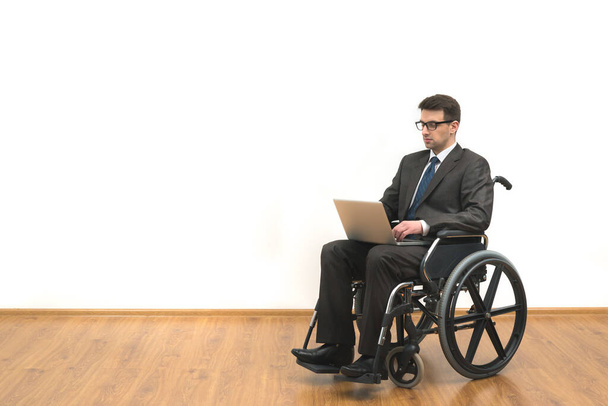 Los discapacitados en la silla de ruedas trabaja con un ordenador portátil en el fondo blanco de la pared - Foto, imagen