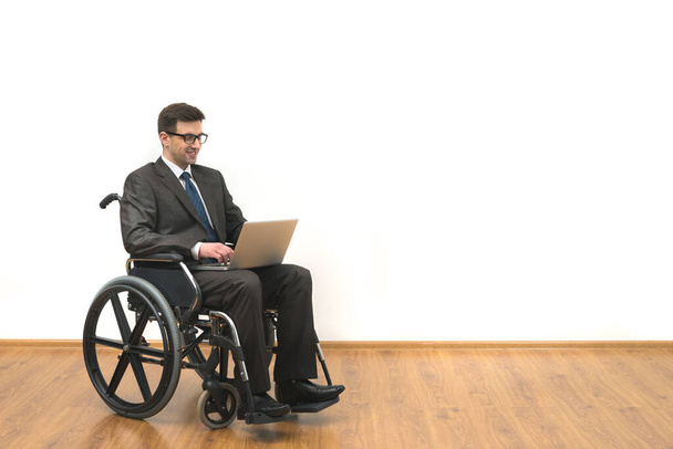 Los discapacitados en una silla de ruedas trabaja con un ordenador portátil en el fondo blanco de la pared - Foto, imagen
