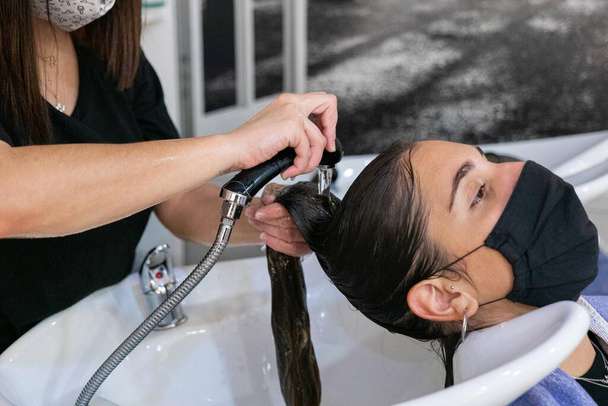 Νεαρή κομμώτρια λούζει τα μαλλιά του πελάτη - Φωτογραφία, εικόνα