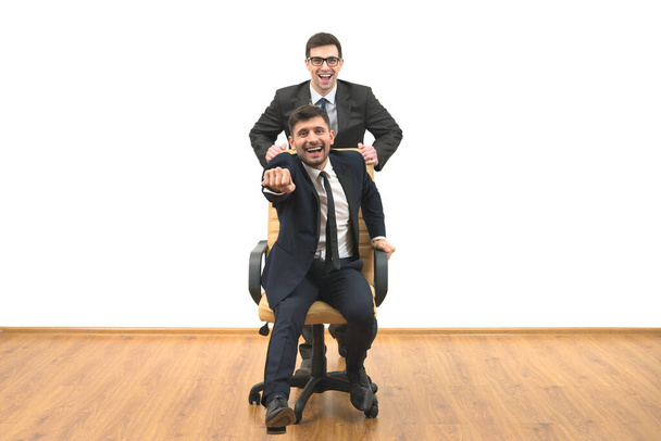 Dva šťastní podnikatelé s židlí zábavu na bílém pozadí zdi - Fotografie, Obrázek
