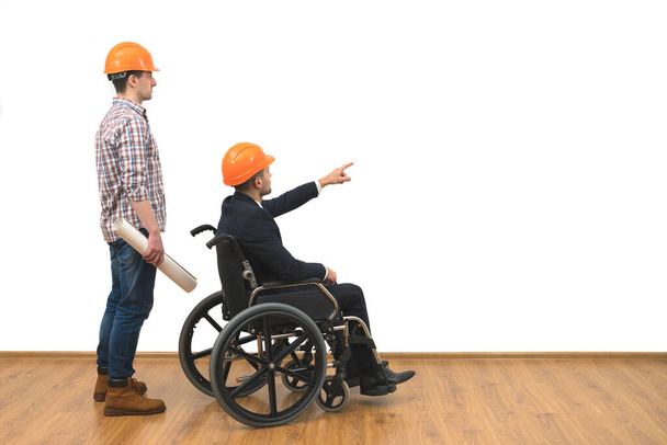 Los dos ingenieros con un gesto de silla de ruedas en el fondo blanco de la pared - Foto, imagen
