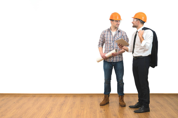 Die beiden Männer in Helmen stehen mit einem Tablet auf dem weißen Wandhintergrund - Foto, Bild