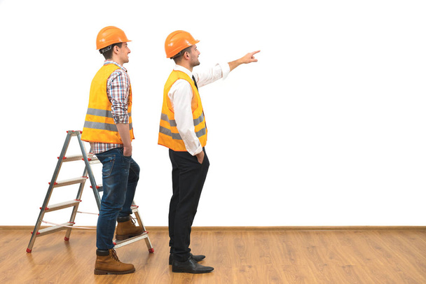 Die beiden Bauarbeiter neben der Leiter gestikulieren auf dem weißen Wandhintergrund  - Foto, Bild