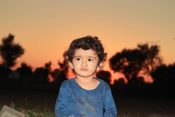 Портретная фотография маленького индийского ребенка, играющего в саду после заката. Прекрасные дети Индии, детство, улыбающееся лицо маленького ребенка, будущее Индии, сегодняшние дети - Фото, изображение