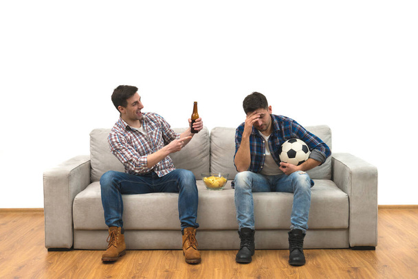 A két srác sörrel és chipsszel focit néz a kanapén. - Fotó, kép