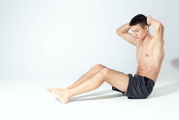 bodybuilder in korte broek doet fitness in een lichte kamer opgeblazen romp - Foto, afbeelding