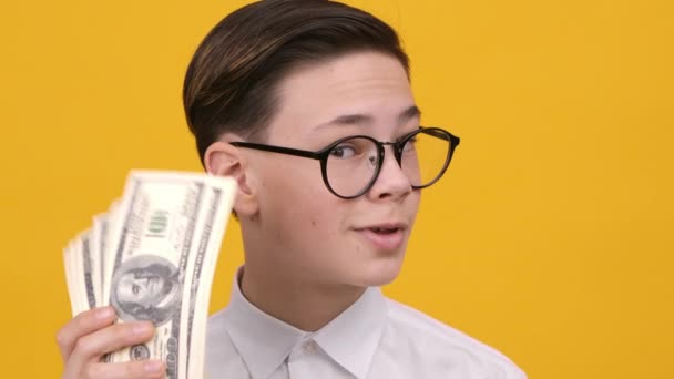 Gazdag tini fiú holding pénz rázás dollár jegyzetek, sárga háttér - Felvétel, videó