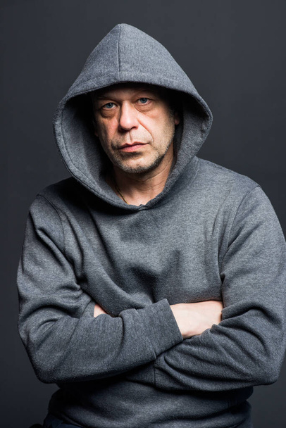 Studio portrait of a 40-50-year-old serious man in a gray hoodie on a neutral background, looking at the camera, eyes swollen. Maybe he's an actor or a truck driver, a lawyer or a retired military man. - Fotoğraf, Görsel