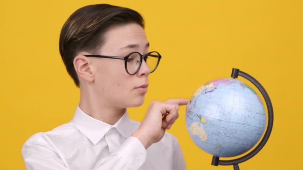 Koulupoika tilalla Earth Globe osoittaa sormella poseeraa yli keltainen tausta - Materiaali, video