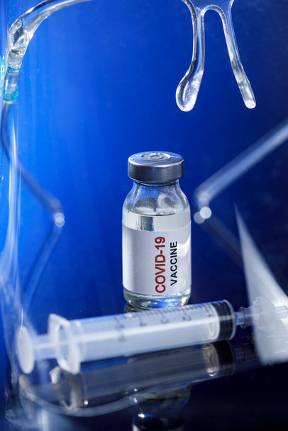 Bir şişe aşı, şırıngalı bir şırınga ve mavi arka planda tıbbi maskeli bir ampul..  - Fotoğraf, Görsel