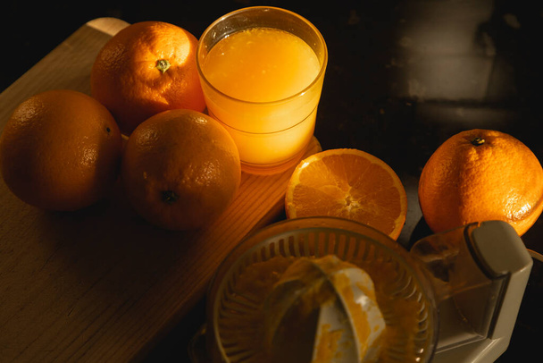 Haciendo zumo de naranja recién exprimido en casa, para un desayuno saludable, mientras las primeras luces de la mañana se cuela en la cocina, sumergiendo todo en un hermoso claroscuro. - Foto, Imagen