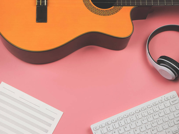 Visão superior ou flat lay de teclado do computador, fones de ouvido, folha de música em branco e guitarra acústica em fundo rosa. Música aprendizagem on-line e conceito músico. - Foto, Imagem