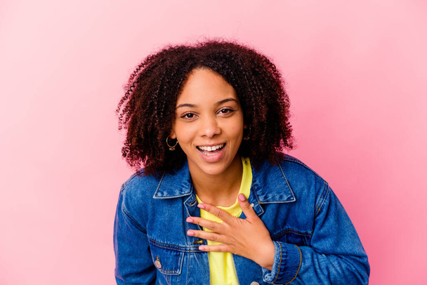Joven afroamericana mixta mujer de raza aislada ríe en voz alta manteniendo la mano en el pecho. - Foto, Imagen