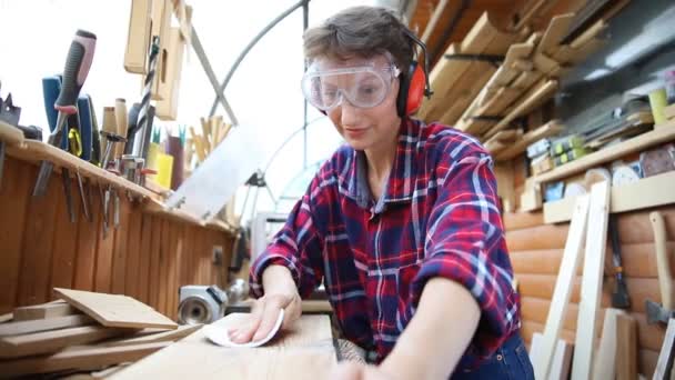 Jeune charpentier professionnel attrayant de 30 à 40 ans qui broie du bois brut avec du papier de verre dans un atelier de menuiserie. Concept d'égalité des femmes féminines. Fille adulte avec passe-temps masculin à l'établi - Séquence, vidéo