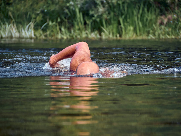 Man swims freestyle in open water on the river in summer - Photo, Image