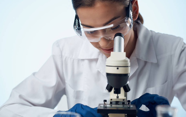 žena lékař v lékařských šatech a mikroskop na stole brýle na obličeji laboratorní výzkum - Fotografie, Obrázek