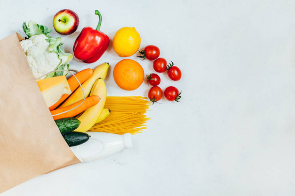 vista dall'alto del sacchetto di carta con frutta, verdura, spaghetti, formaggio, latte su sfondo bianco - Foto, immagini