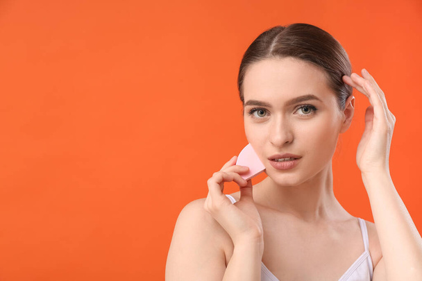 mooie jonge vrouw met make-up spons op kleur achtergrond - Foto, afbeelding