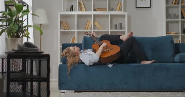 verdriet van liefde en romantische gevoelens van jonge vrouw spelen gitaar, dame ligt op de bank in appartement en het maken van muziek - Video