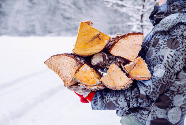 冬の屋外で彼女の膝の上に薪の山を運ぶ女性の詳細は、農村部の自然。北欧の冬のライフスタイルコンセプト. - 写真・画像