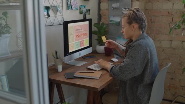 Средний снимок молодой женщины с дредами, сидящей за столом с компьютерными покупками в Интернете, вводящей информацию о кредитной карте на веб-сайт для оплаты - Кадры, видео