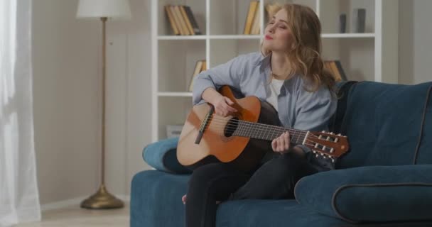 Ευτυχισμένη νεαρή γυναίκα παίζει κιθάρα στο σπίτι το Σαββατοκύριακο, περνώντας χρόνο στο σαλόνι, κάνοντας μουσική, χόμπι - Πλάνα, βίντεο
