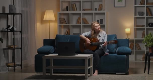 teen girl is playing guitar and suffering about love, sitting alone at home at evening, music and creative hobby - Footage, Video