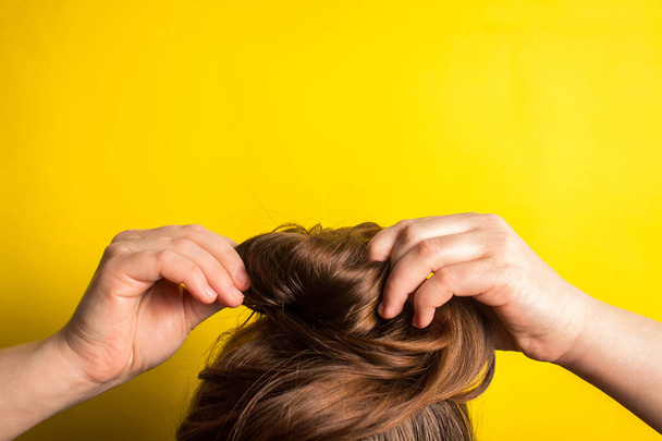 Een vrouw maakt een rommelig haarbroodje op haar hoofd. Gele achtergrond. Begrepen, ruimte. Trend kleur van het jaar 2021 - Foto, afbeelding