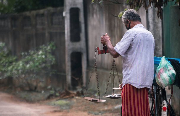 Pescadores enmascarados Mano sosteniendo una balanza, equilibrando los peces y el peso, forma típica de medir el peso de los peces en las principales partes de Sri Lanka. La nueva forma normal de hacer negocios. - Foto, Imagen