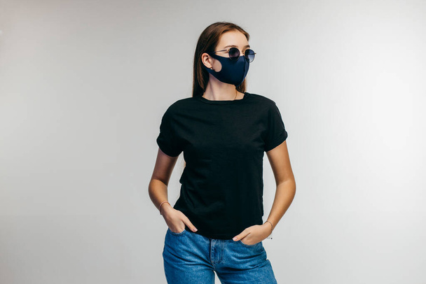 Tyylikäs tyttö lasit ja naamio yllään musta t-paita poseeraa studiossa sinisellä pohjalla - Valokuva, kuva